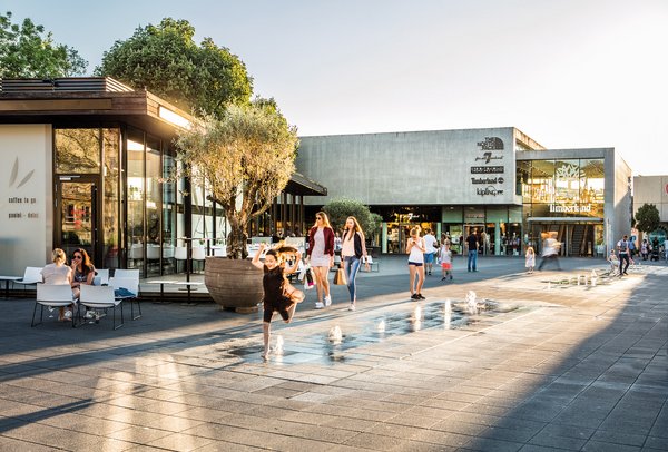 Kinder rennen bei Abenddämmerung lachend über einen Platz mit Brunnen
