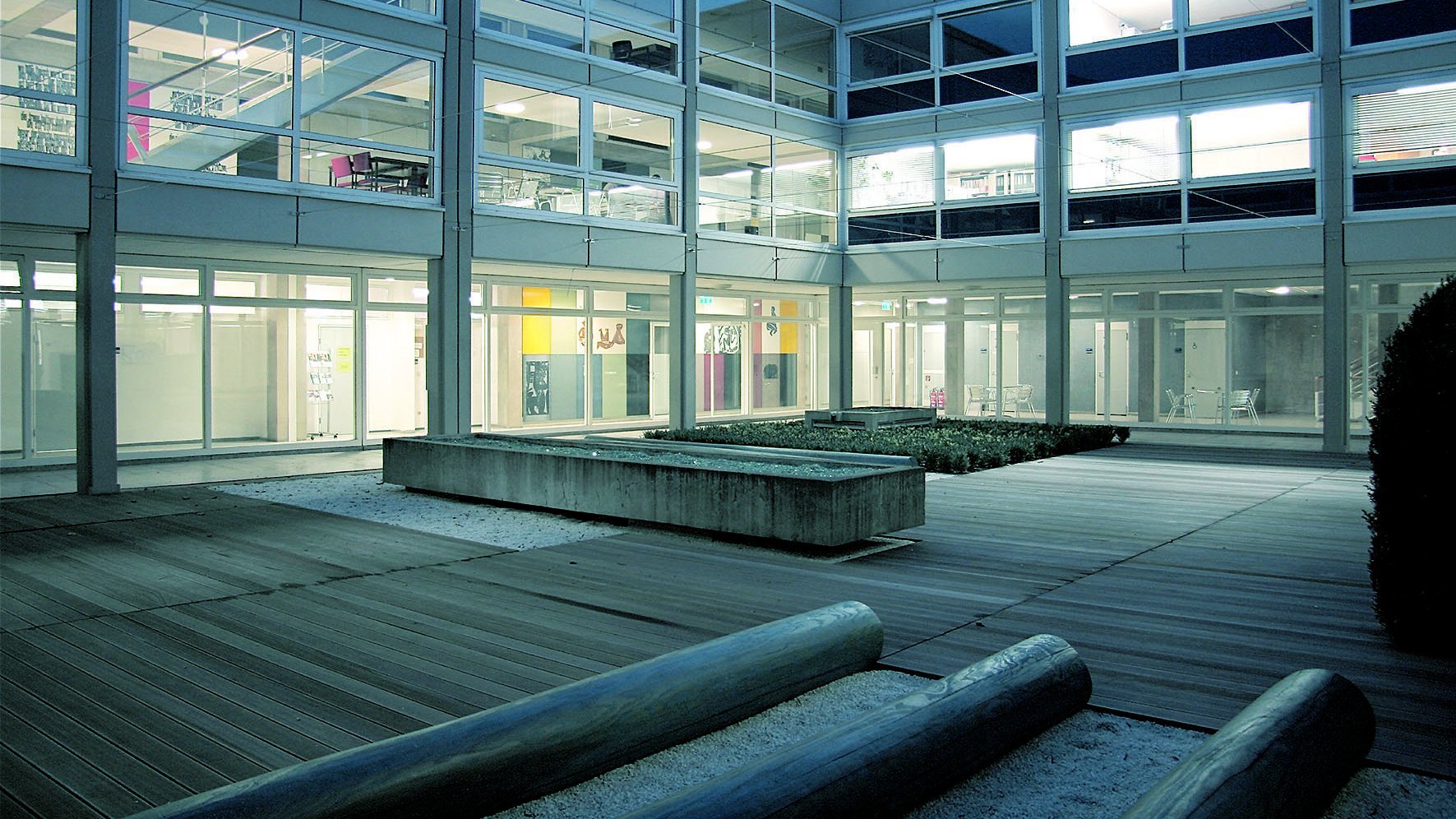 Innenhof eines Glasbaus mit Sitzgelegenheiten bei Abendlicht